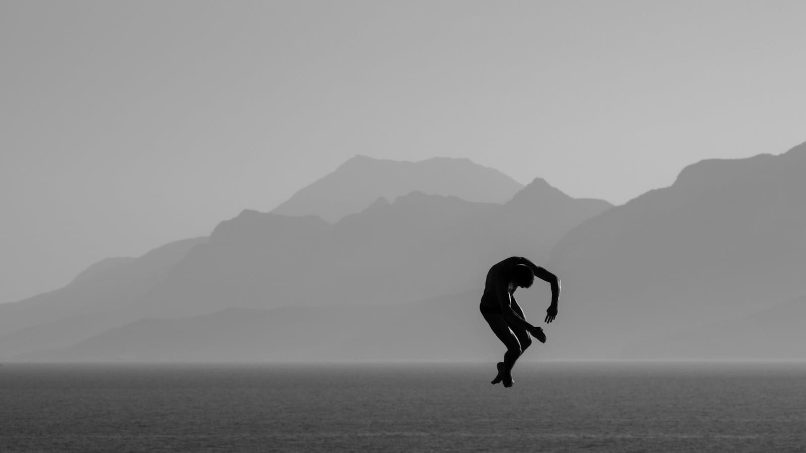 Silhouette of a man diving over the sea with mountains in the background in Antalya, Türkiye.