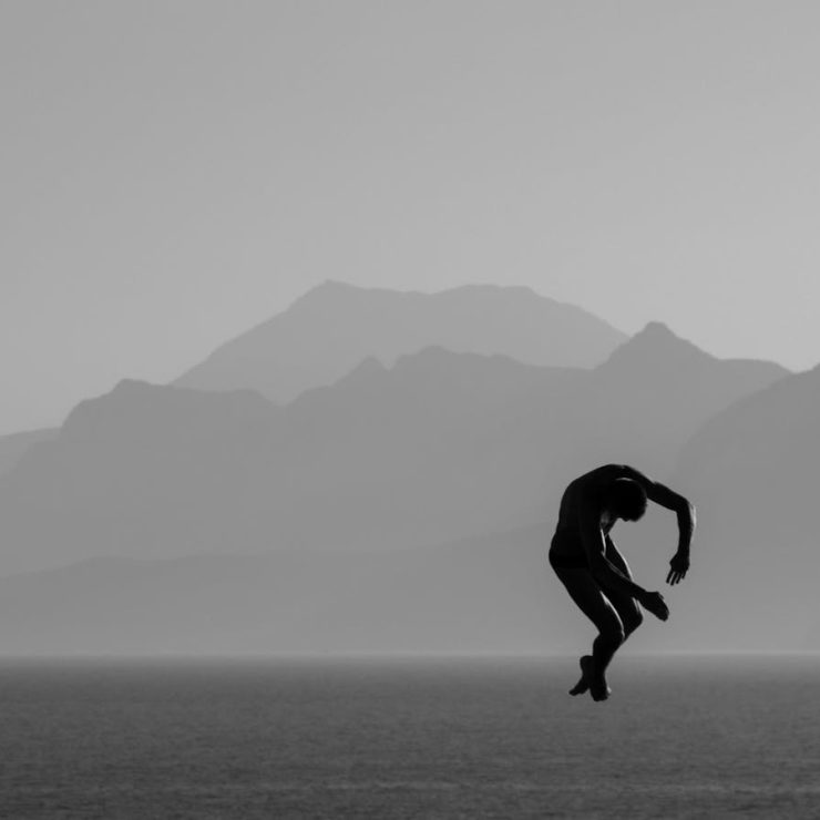 Silhouette of a man diving over the sea with mountains in the background in Antalya, Türkiye.