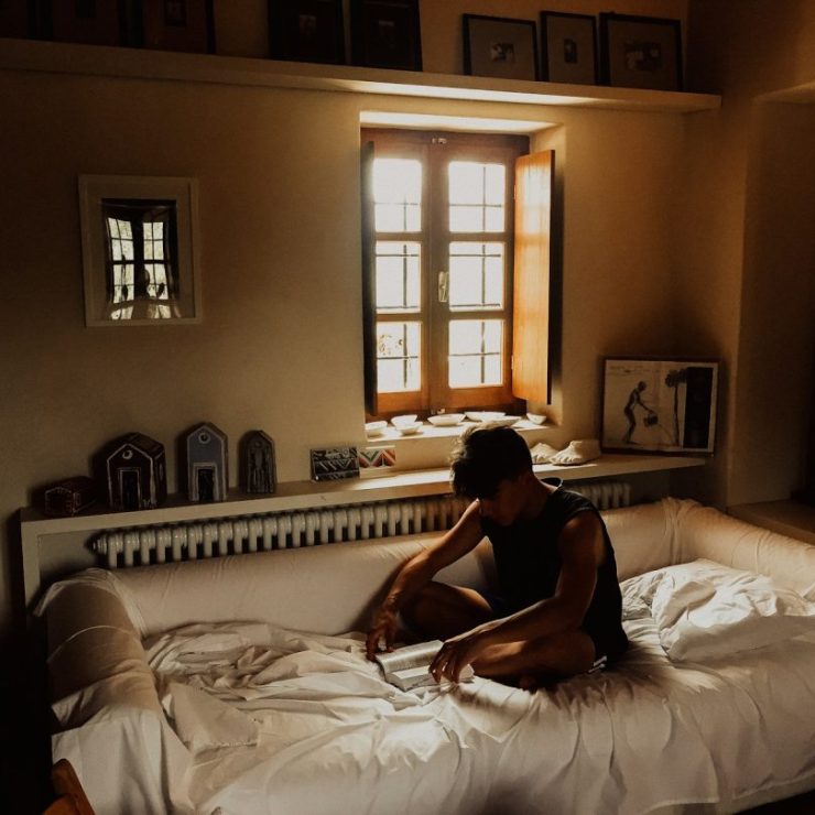 man sitting on bed beside opened window