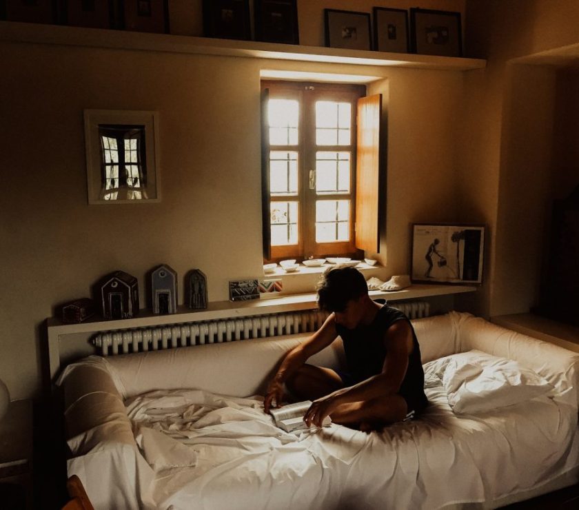 man sitting on bed beside opened window