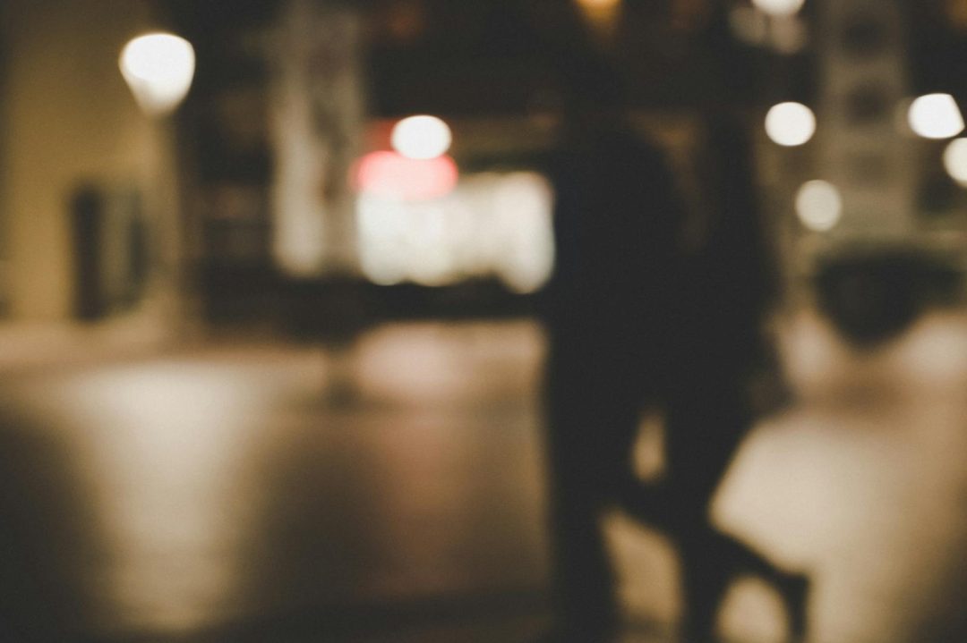 Out-of-focus image of a couple walking at night with city lights in the background.