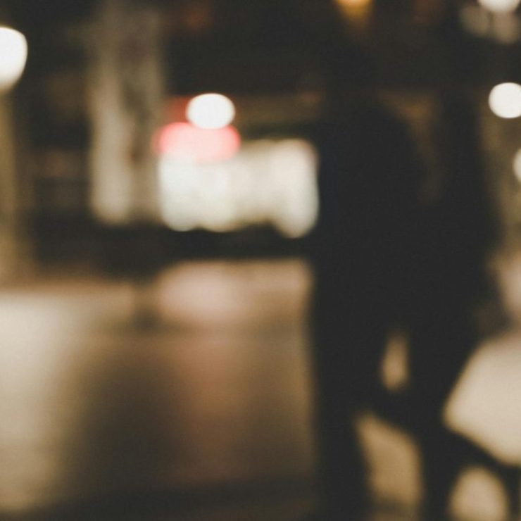Out-of-focus image of a couple walking at night with city lights in the background.