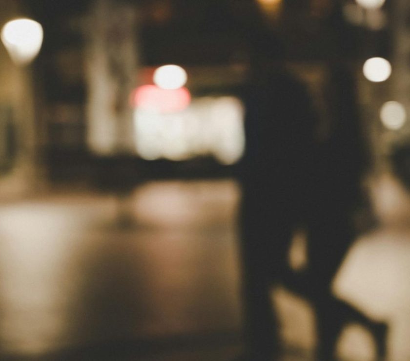 Out-of-focus image of a couple walking at night with city lights in the background.