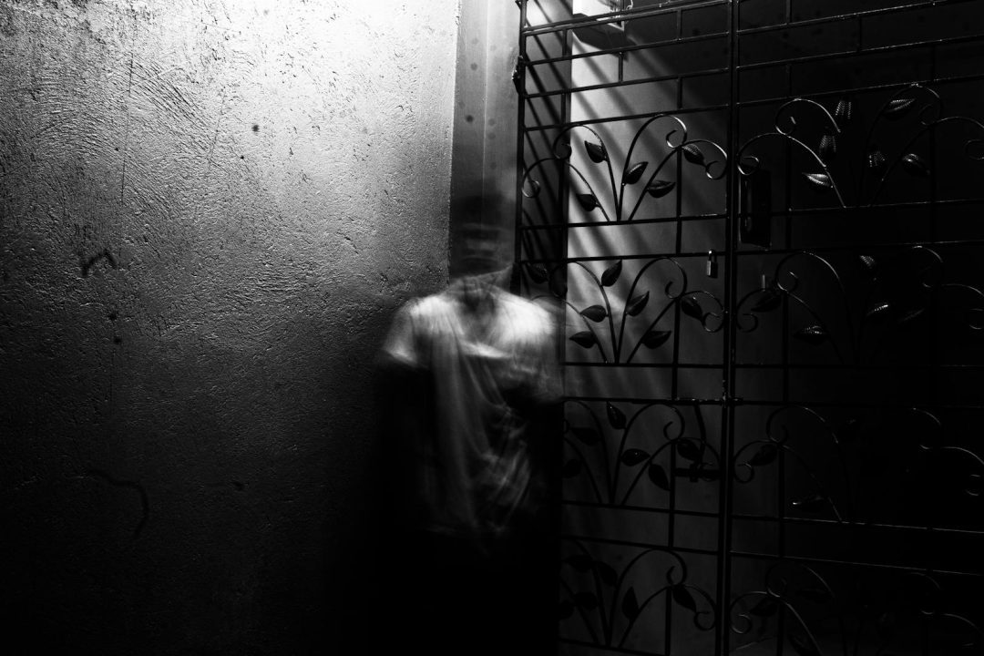 Grayscale photo of a blurred figure in an eerie indoor setting with metalwork.