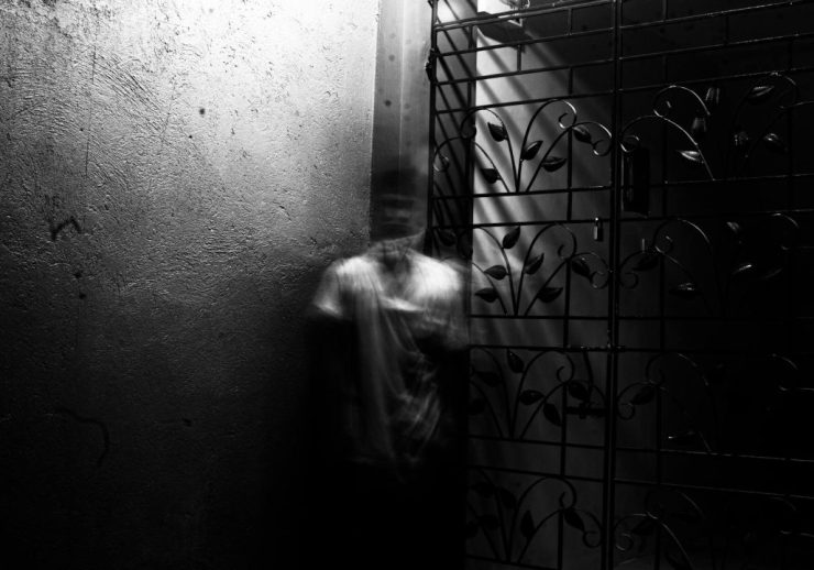 Grayscale photo of a blurred figure in an eerie indoor setting with metalwork.