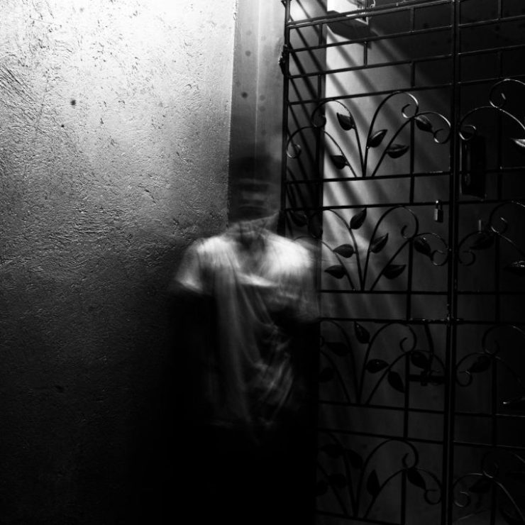 Grayscale photo of a blurred figure in an eerie indoor setting with metalwork.