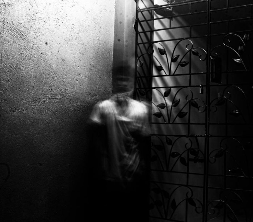 Grayscale photo of a blurred figure in an eerie indoor setting with metalwork.