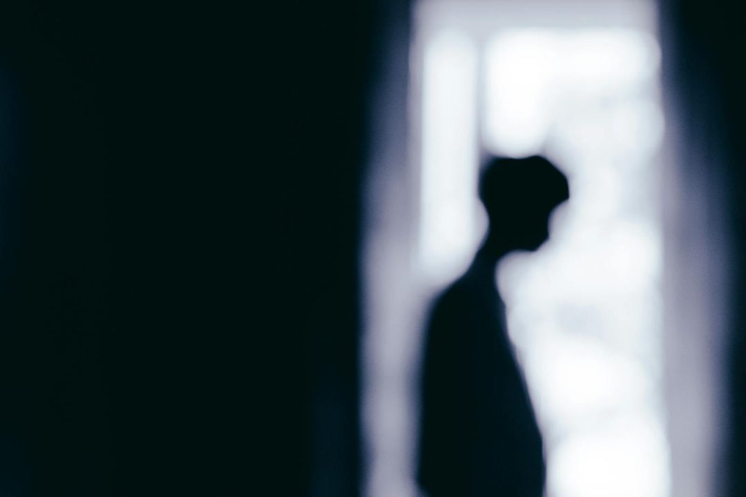Blurred silhouette of a person standing near a window, creating a moody atmosphere.