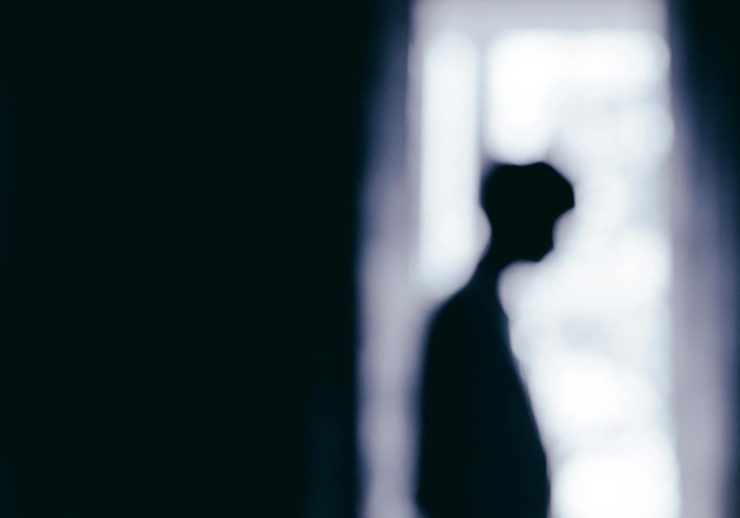 Blurred silhouette of a person standing near a window, creating a moody atmosphere.