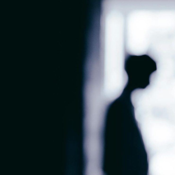 Blurred silhouette of a person standing near a window, creating a moody atmosphere.