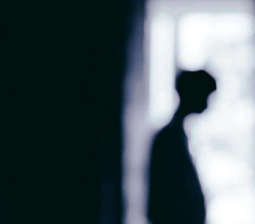 Blurred silhouette of a person standing near a window, creating a moody atmosphere.